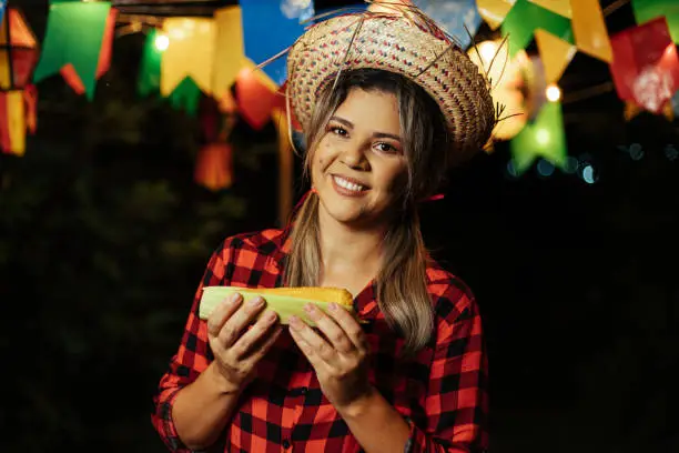 Photo of Brazilian woman wearing typical clothes for the Festa Junina - June festival - eating corn on the cob