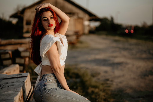 Beautiful young adult posing in ballet shoes with gorgeous outfit, jeans and white crop top. Little makeup and curly red hair. Posing in standing and sitting poses. Well designed photography with sunrays.