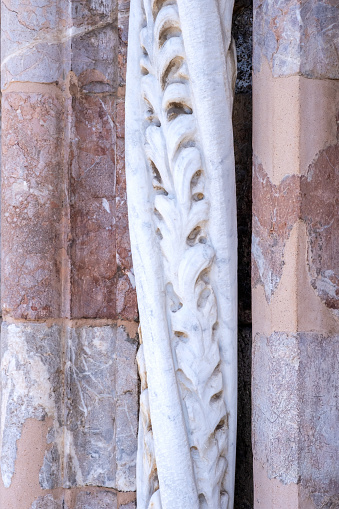 Marble details on facade of Messina Cathedral or Duomo di Messina, Sicily, Italy. Carved stone columns and reliefs, pink marble wall. Decorative elements in architecture.