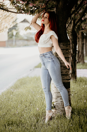 Beautiful young adult posing in ballet shoes with gorgeous outfit, jeans and white crop top. Little makeup and curly red hair. Posing in standing and sitting poses. Well designed photography with sunrays.