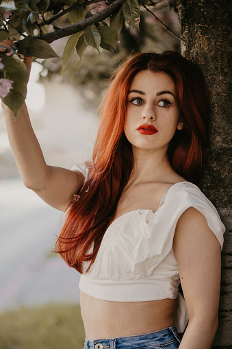 Beautiful young adult posing in ballet shoes with gorgeous outfit, jeans and white crop top. Little makeup and curly red hair. Posing in standing and sitting poses. Well designed photography with sunrays.