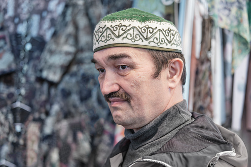 Close-up portrait in profile of senior Asian man wearing skullcap made of soft felt and decorated with national ornaments. Kyrgyz headdress topu.