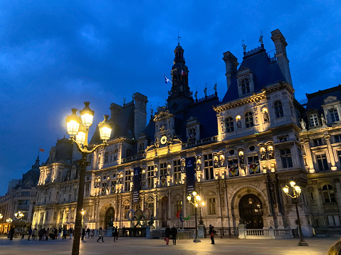 The Hotel de Ville at night with lights on, against dark blue sky.