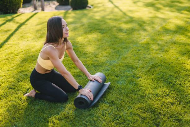 istock Woman rolling black exercise mat on park grass after finishing her training session. Equipment for fitness, pilates, yoga. Well being concept. 1485189857