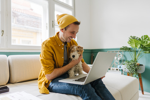 Photo of a man with his dog, finishing some tasks on his laptop inside his home-based office.
