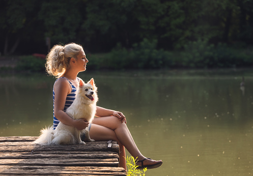 Middle age woman enjoying time with her dog near the lake at sunset