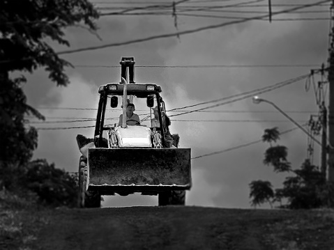 Countryman driving a tractor for agriculture. The photo was taken in a rural area away from the city center and is in black and white.