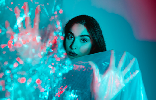 High Fashion model woman in colorful bright neon blue and purple lights posing in studio. Portrait of beautiful girl with trendy glowing make-up. Art design vivid style