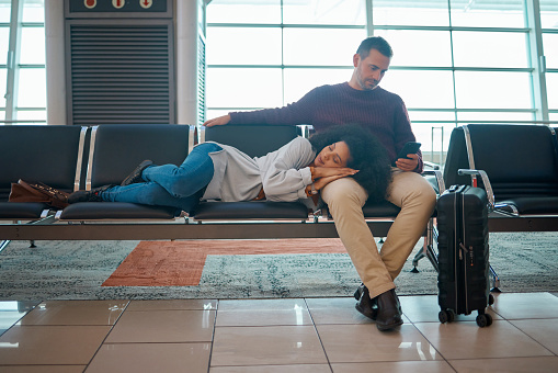 Airport, sleeping woman and couple waiting for airplane for holiday travel together.Tired, flight delay and luggage of people going on a international vacation journey with suitcase on a chair