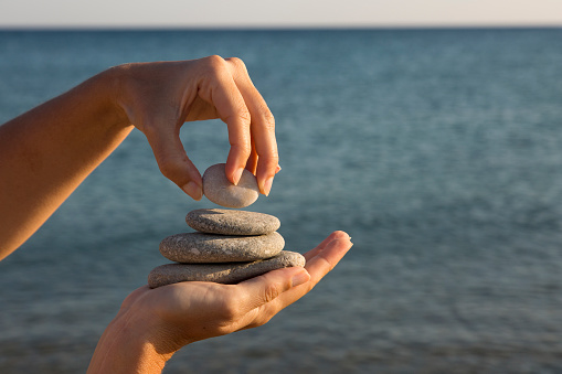 Stack pebbles rising in a pyramid shape in woman's hand, sea background. Personal growth, success, motivation, meditation and Zen concepts. Horizontal close-up.