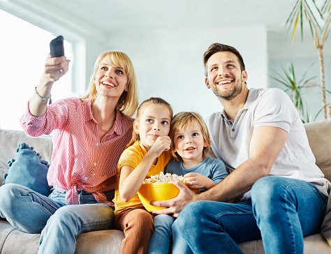 Family having fun watching tv and eating pop corn on sofa at home