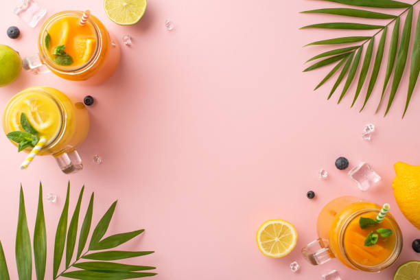空のスペースを持つスタイリッシュなピンクの背景にヤシの葉で飾られたオレンジ、レモン、ライムで作られた柑橘系のカクテルのこのトップビューフラットレイで夏の味を解き放ちます - cocktail orange cup juice ストックフォトと画像
