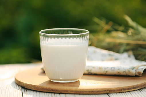 Glass of tasty fresh milk on white wooden table against blurred background