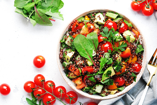 Quinoa tabbouleh salad with red cherry tomatoes, orange paprika, avocado, cucumbers and parsley. Traditional Middle Eastern and Arabic dish. White table background, top view