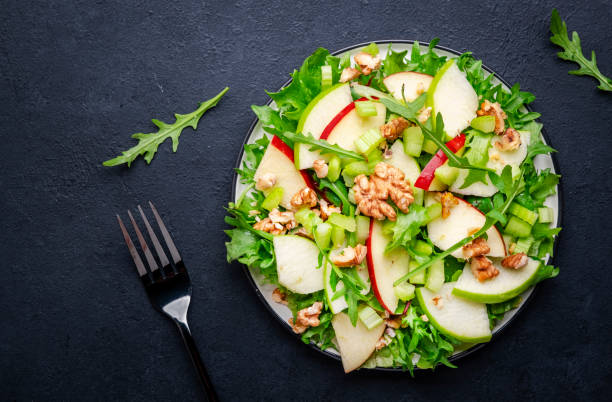 istock Waldorf salad with red and green apple, celery, lettuce, arugula and walnuts on plate, black table background, top view 1485226102
