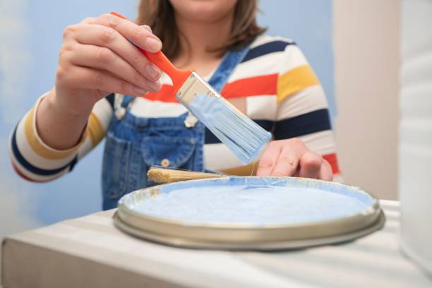 woman's hand taking out a brush with blue paint from a tray