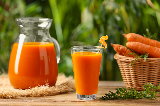 Tasty juice and carrot on wooden table outdoors