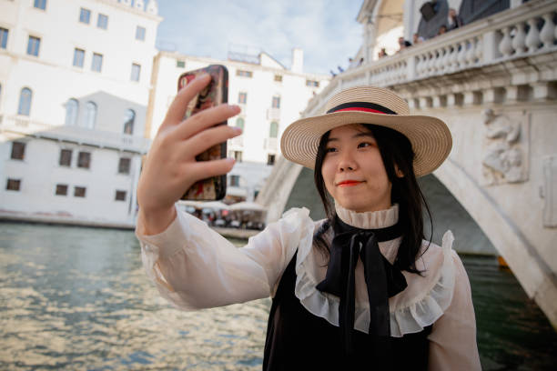 a chinese tourist takes a selfie in front of the rialto bridge in venice - venice italy rialto bridge tourist architecture imagens e fotografias de stock