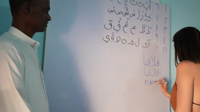 Teacher teaching tourist woman how to write in arabic language during lecture in the classroom