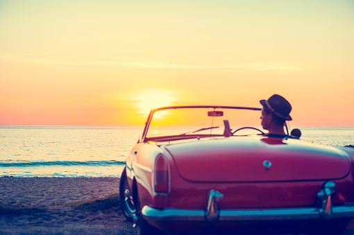 Mature man driving a convertible car at the beach. The car is a vintage model shot at sunset or sunrise. The man looks happy and could be on vacation or having an adventure. He is texting on a mobile phone. Rear view defocussed with copy space\n\nNote to inspector regarding convertible car images:\n\nIn planning for the shoot that includes these car shots, I requested some information on the Getty forums regarding car copyright and received the following from Donald Gruener:\n\n\