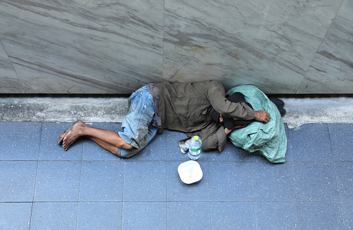 Homeless man sleeping on footpath seeking help from people walking pass.
