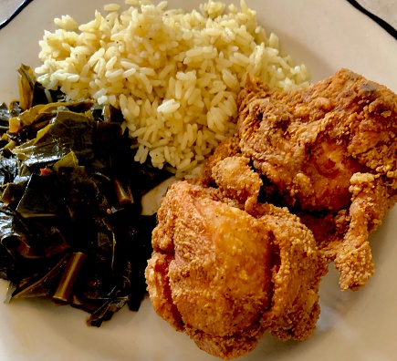 A mouth-watering meal of collard greens, rice, and crispy fried chicken served on a white plate in a popular Southern style food cuisine restaurant in the Upper West Side of Manhattan in New York City.