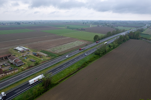 Piacenza, Italy - April 2023 Cargo trucks and cars in the motorway a1 autostrada del sole aerial point of view in between padain plain rural fields
