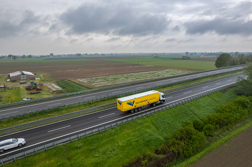 Piacenza, Italy - April 2023 Cargo trucks and cars in the motorway a1 autostrada del sole aerial point of view in between padain plain rural fields