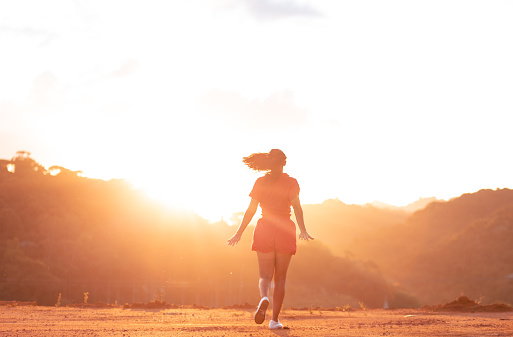 Happy woman with open arms and running outdoors with sunset in background