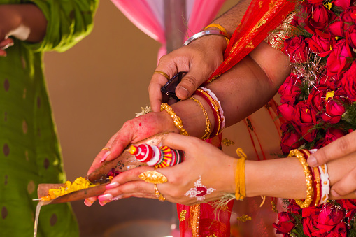 Hindu bengali marriage rituals being performed when bride and groom pouring gangajal on holy fire. Hands of the bride and groom seen in traditional attire during wedding or matrimonial occassion.