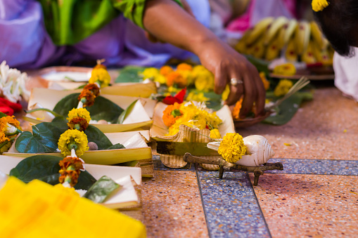 Hindu puja rituals being performed with flowers in front of priest during pooja, wedding, funeral ceremonies. Miscellaneous religious essentials are kept in front. A person is folding hands to worship