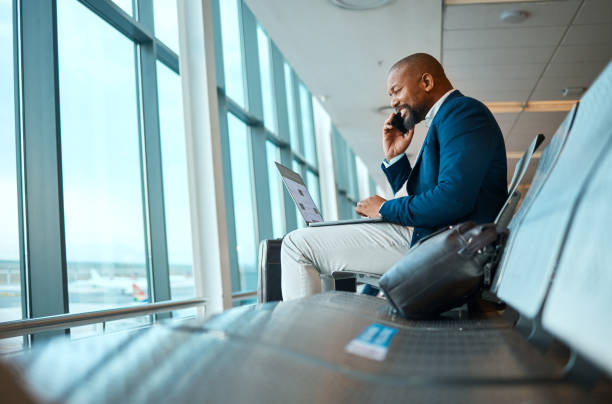 rozmowa telefoniczna, podróż i biznesmen na laptopie na lotnisku do pracy wyjazd firmowy w mieście. technologia, komunikacja i afrykański pracownik na rozmowie mobilnej czeka na wejście na pokład samolotu - commercial airplane airport arrival departure board business travel zdjęcia i obrazy z banku zdjęć