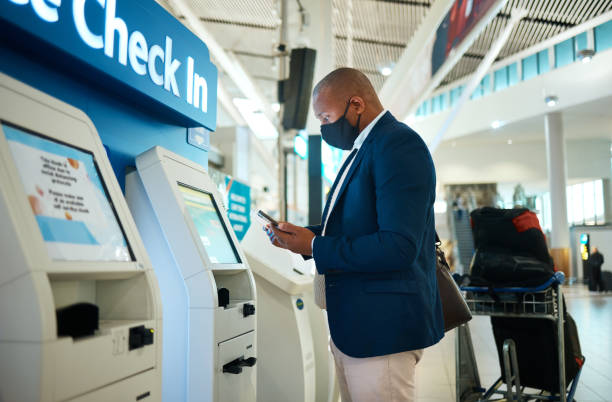 Black man, face mask and plane self check in with phone app with airport information for travel. International flight data, businessman and luggage of a employee reading mobile info for airplane hombre negro, máscara facial y auto check-in de avión con la aplicación de teléfono con información del aeropuerto para viajar. datos de vuelos internacionales, hombre de negocios y equipaje de un empleado leyendo información móvil para avión