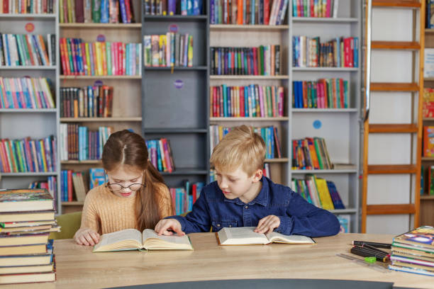 istock Schoolchildren reading books together while sitting at table in library. Back to school 1485263581