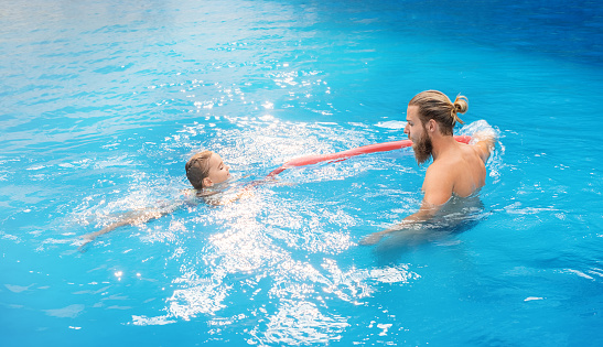 Father teaches child to swim in the pool with a stick