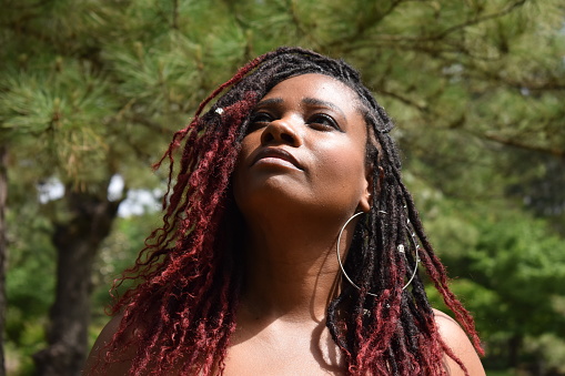A beautiful model of color with a rare ruby red dyed and African braided hairstyle, looking up with trees in the background.
