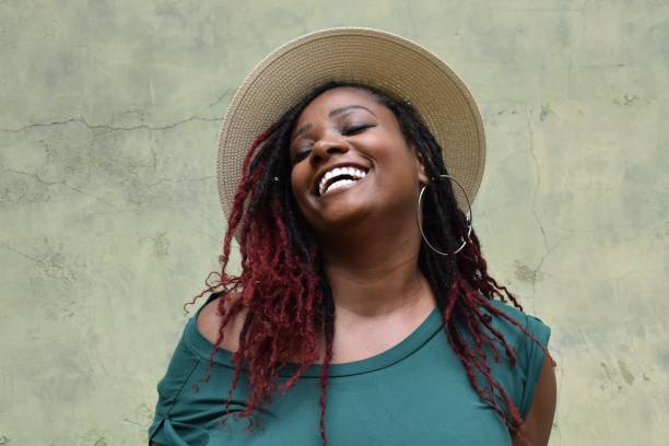 A portrait of a laughing yet beautiful model of color with a rare ruby red dyed and African braided hairstyle, with a sun hat and large silver earing. A portrait of a beautiful model of color with a rare ruby red dyed and African braided hairstyle, with a sun hat and large silver earing. plus size woman fashion laughing stock pictures, royalty-free photos & images