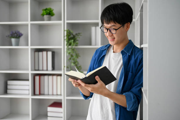 istock Young Asian college student with glasses reading book in the study room 1485272449