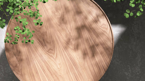 istock Modern, minimal teak wood round smooth beautiful grain podium table, green tropical tree in sunlight, leaf shadow on blank concrete floor 1485277424