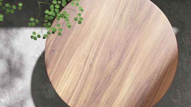 Modern, minimal teak wood round smooth beautiful grain podium table, green tropical tree in sunlight, leaf shadow on blank concrete floor stock photo