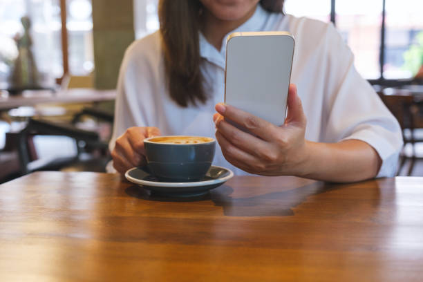 istock Closeup image of a young woman holding and using mobile phone while drinking coffee in cafe 1485282236