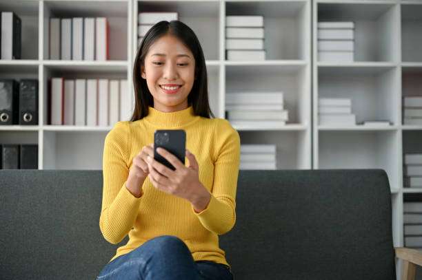istock Cheerful young Asian woman using smartphone while sitting on the sofa 1485287875