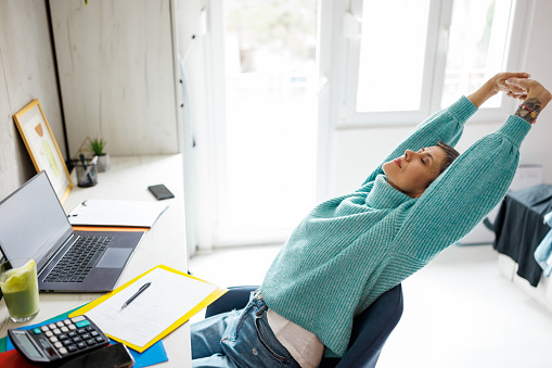 Mature woman stretching while working on laptop from home office