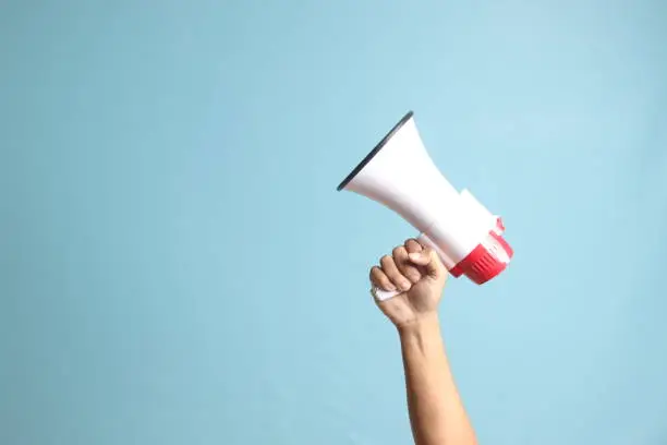 Photo of male hand holding megaphone, announcing advertisement. Isolated image on blue background