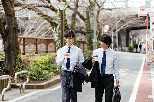 Two young businessman men walking with a take -out cup while talking