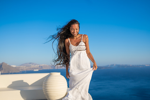 Young female asian woman with white dress on a vacation in Santorini, posing for a picture on a traditional greek background