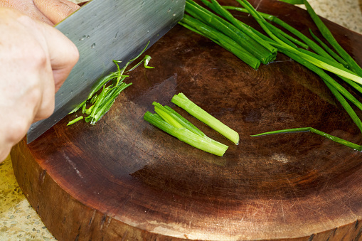 A chef in a Chinese kitchen is cutting green onions