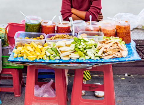 Tasty morsels including mango,papaya,dates and a variety of spicy sauces,on display,for passing pedestrians,on a small colorful stall on the river wall at sunset.
