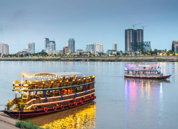 barcos de cruzeiro do rio turístico, iluminado ao entardecer, esperam os clientes, phnom penh, camboja. - phnom penh - fotografias e filmes do acervo