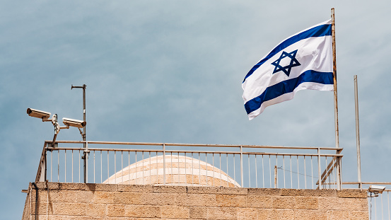 Israeli National Flag blowing in the wind on rooftop in Jerusalem Old City. Surveillance Security Cameras filming the situation around the Jerusalem Old Town and Wailing wall for security and counter terrorism activities. Old City Jerusalem, Israel, Middle East.